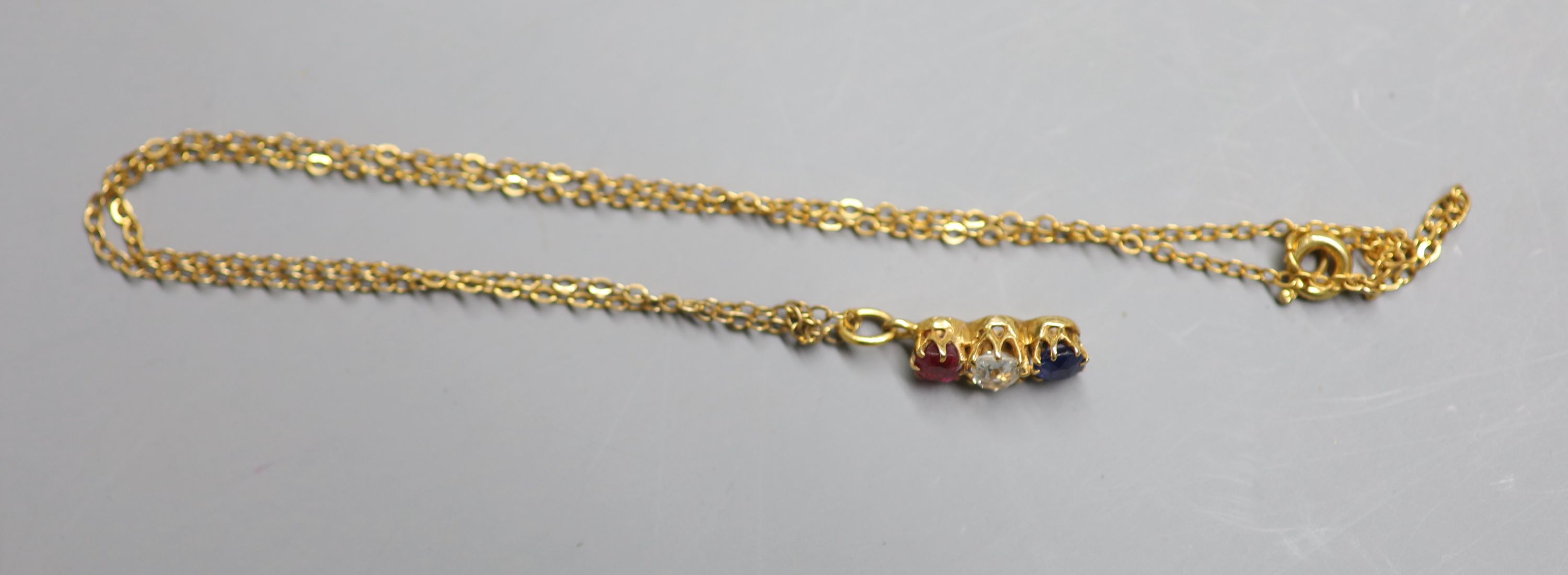 A yellow metal, ruby, diamond and sapphire set line pendant, 14mm, on a yellow metal chain, 38cm, gross 2.4 grams,